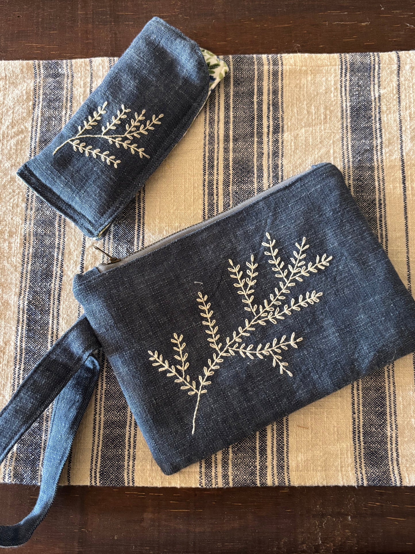 Blue clutch and matching pouch with leaf design on a striped fabric surface