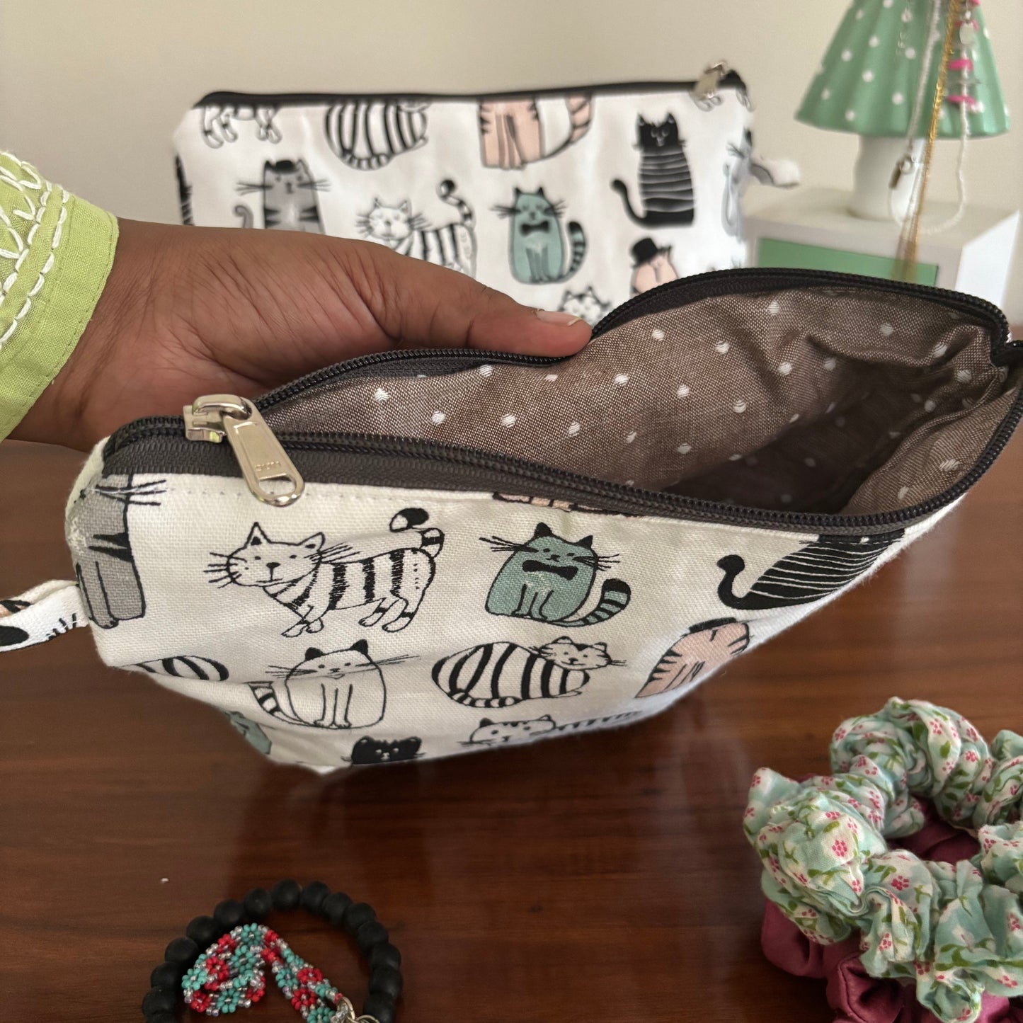 Hand holding a pouch with cat pattern on a wooden surface with hair accessories.