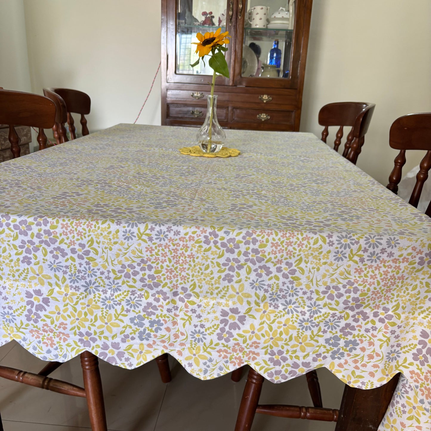 Floral-patterned tablecloth with scallop edges on a wooden dining table with chairs.