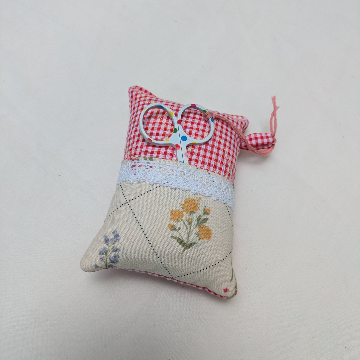 Small fabric pincushions with floral patterns and a pair of scissors on a white background