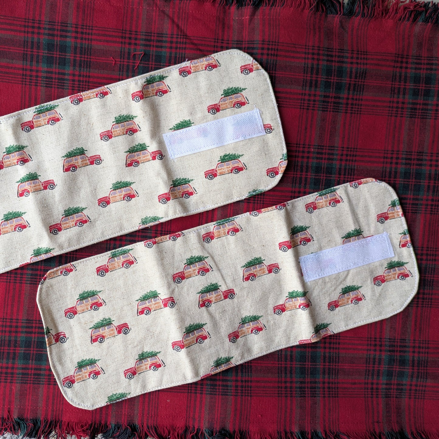 Two fabric car seat covers with Christmas tree and truck pattern on a red plaid background.