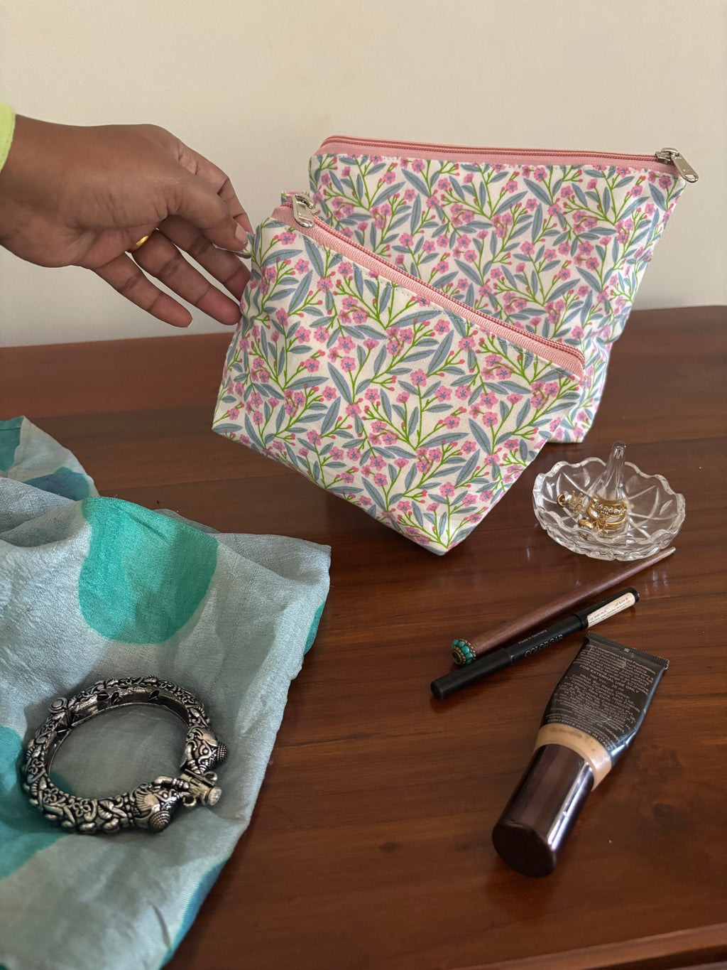 Hand holding a floral pouch over a wooden surface with makeup items.