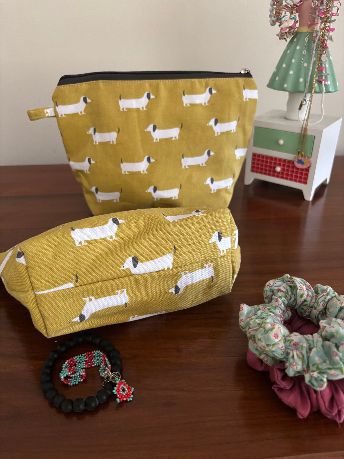 Two yellow pouches with dog pattern on a wooden surface, surrounded by decorative items.