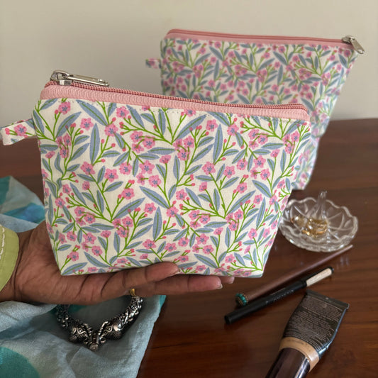 Floral-patterned pouch held by a hand with makeup items on a wooden surface.