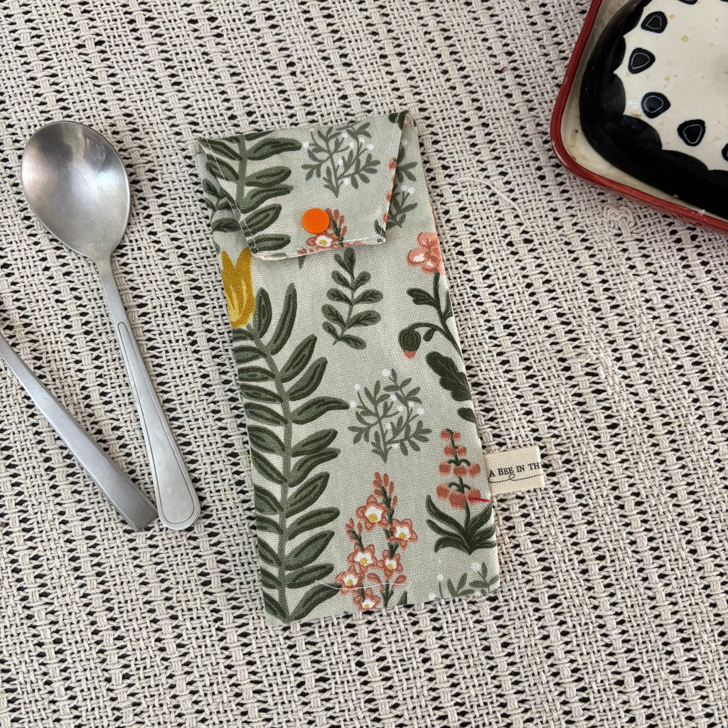 Floral-patterned pouch on a textured surface with spoons and a dish in the background
