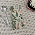 Floral-patterned pouch on a textured surface with spoons and a dish in the background