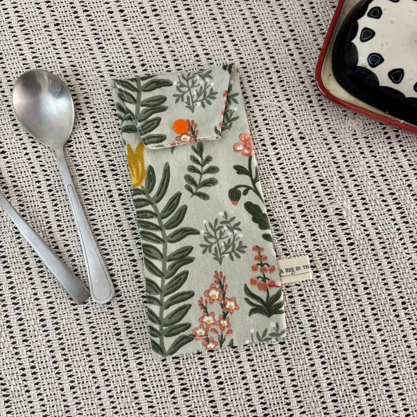 Floral-patterned pouch on a textured surface with spoons and a dish in the background