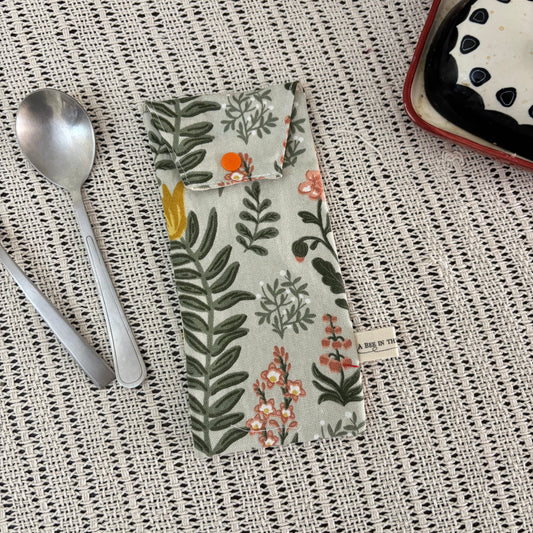 Floral-patterned pouch on a textured surface with spoons and a dish in the background