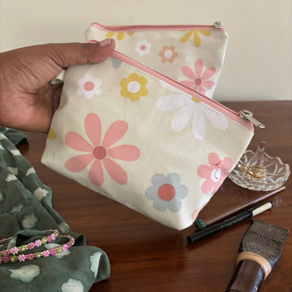 Floral-patterned pouch held by a hand with makeup items on a wooden surface
