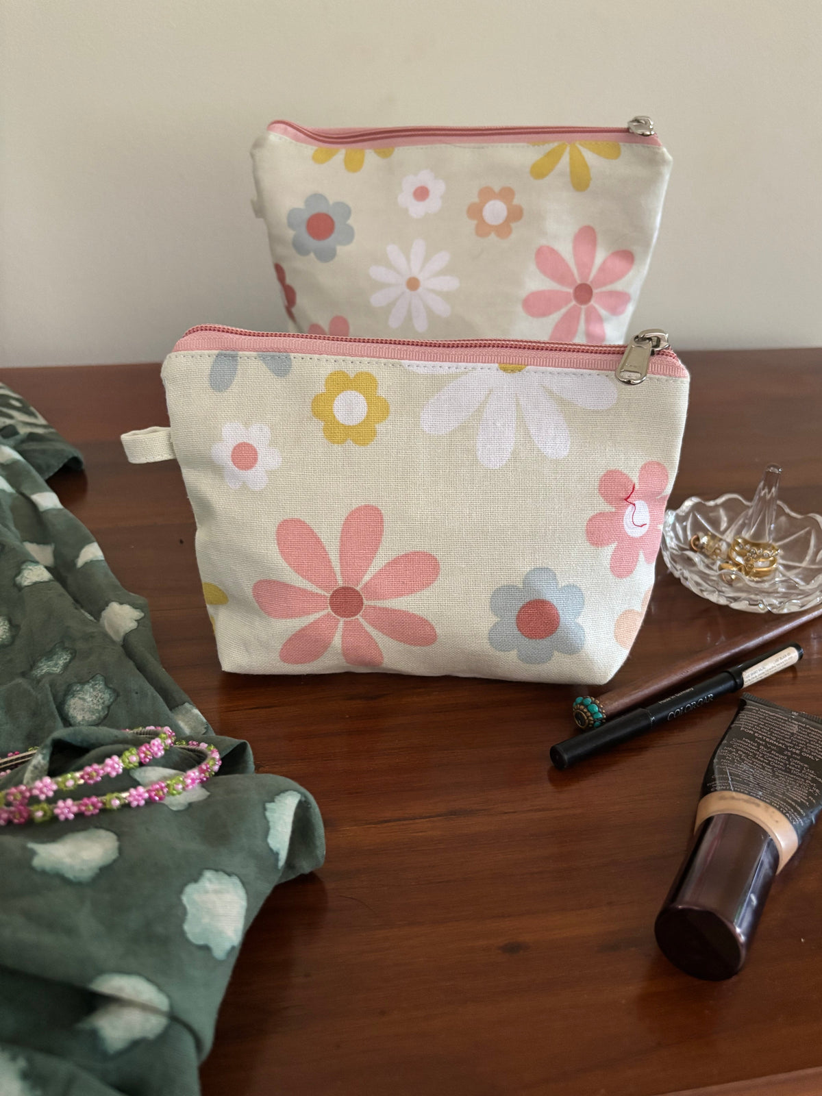 Floral-patterned pouches hanging on a wooden surface with makeup items.