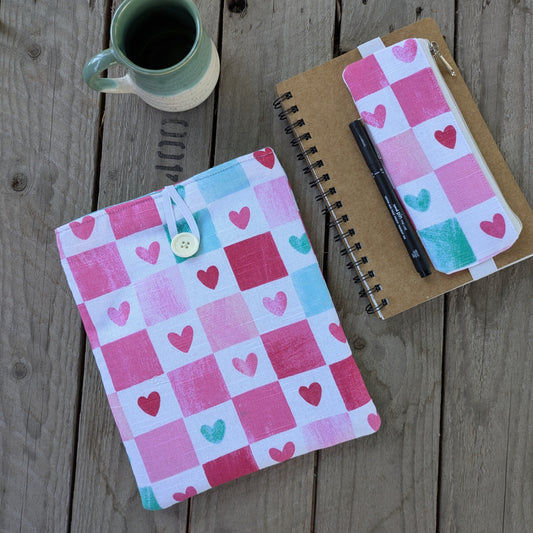 A set of objects - one otbook with an elastic pen pouch along witha book sleev is on a study table with a mug of coffee and a pen. looks like a staionery and book lovers table.