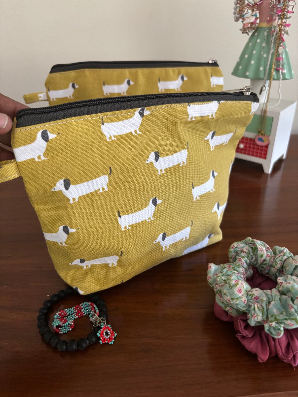 Yellow pouch with dog pattern held by a hand, with scrunchies in the background.