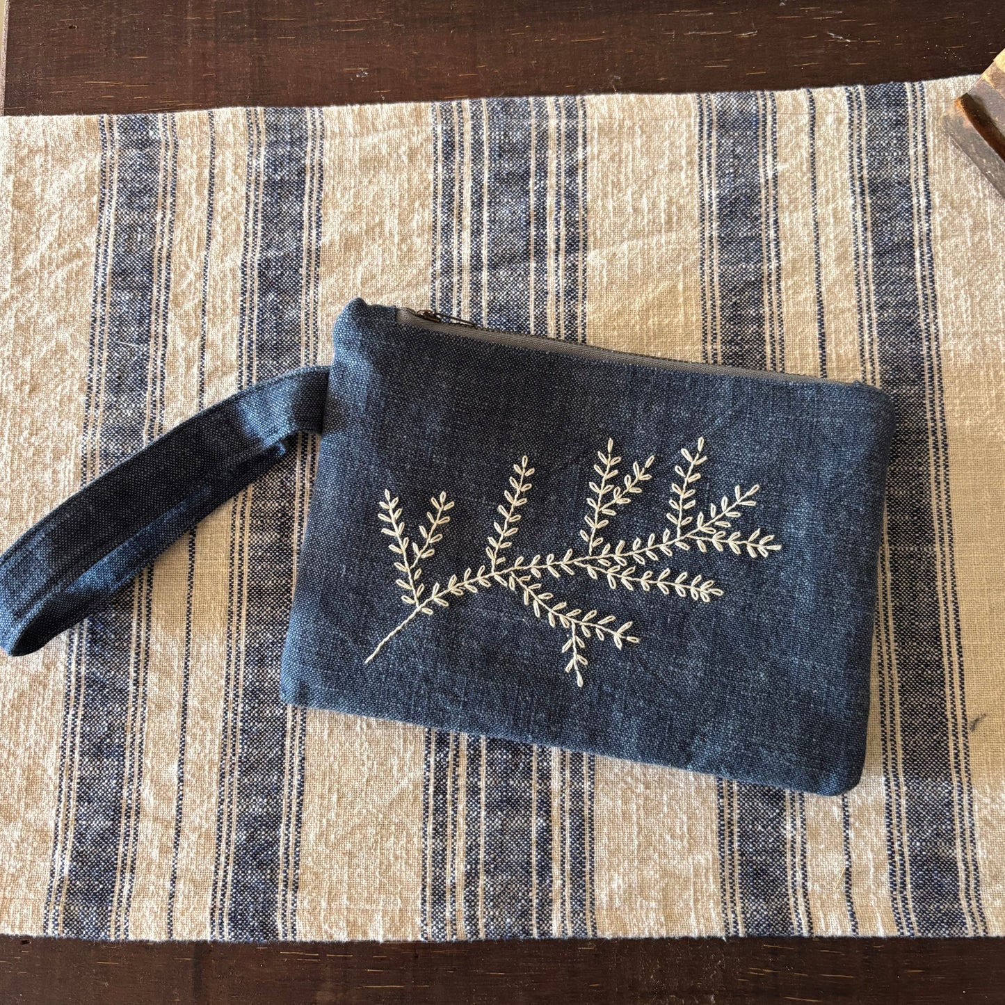 Blue pouch with floral embroidery on a striped fabric surface