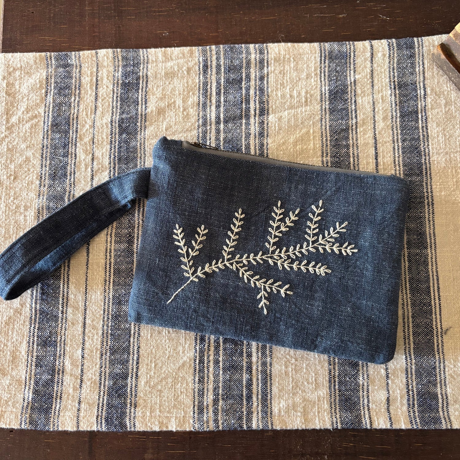 Blue pouch with floral embroidery on a striped fabric surface