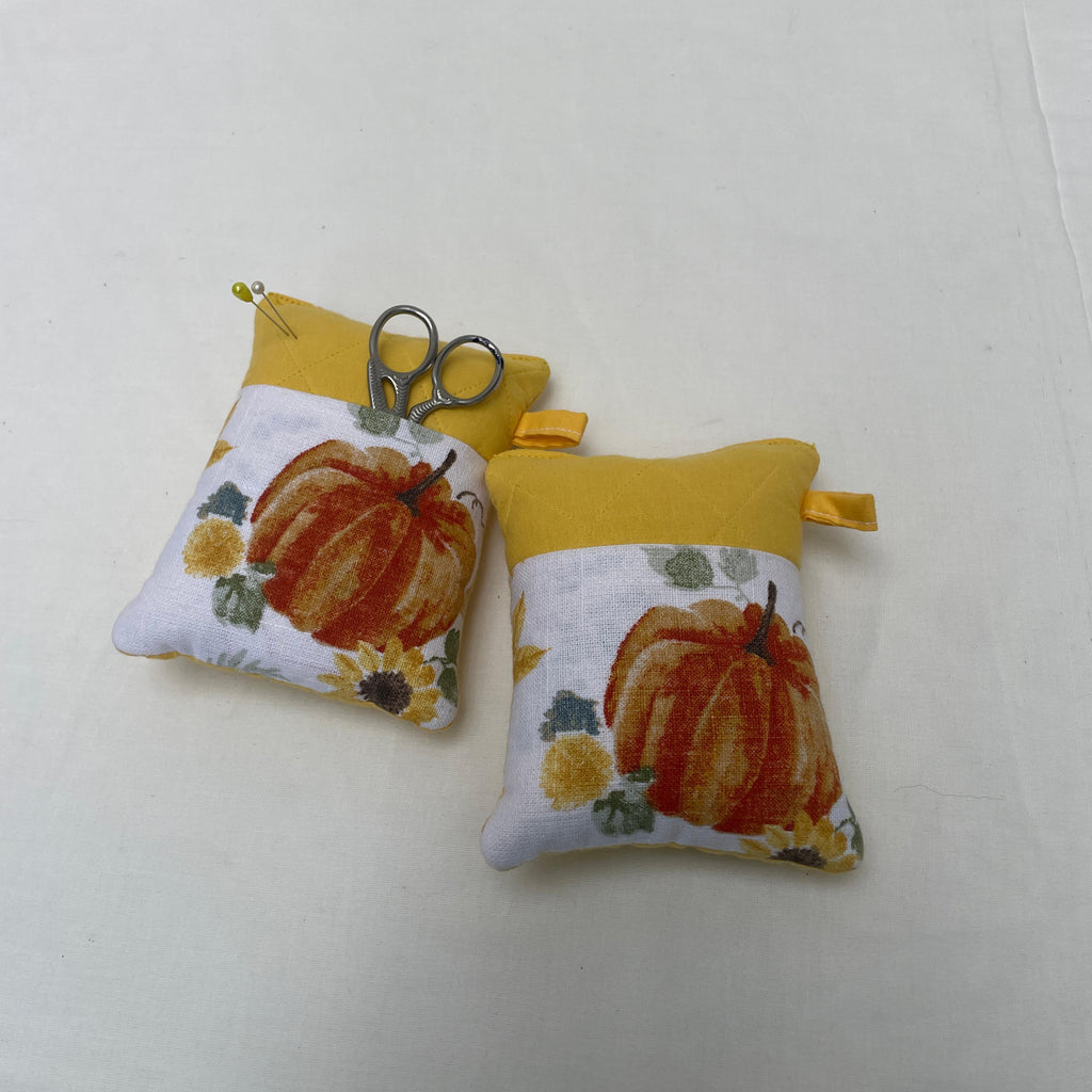 Two fabric pincushions with pumpkin designs on a white surface.