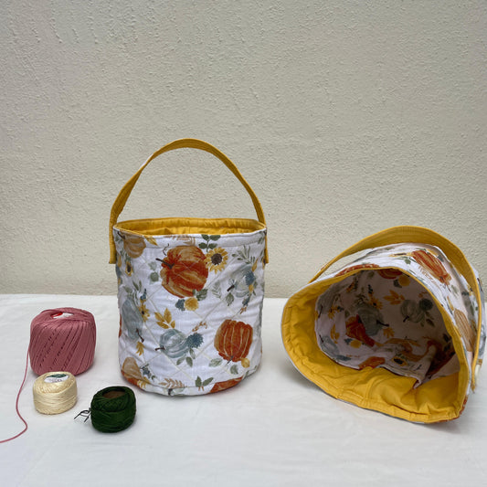 Fabric bucket with floral pattern and yellow handle on a white surface with spools of thread.