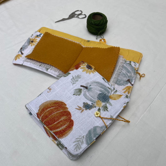 Two fabric needle books with pumpkin designs on a white surface, accompanied by scissors and thread.