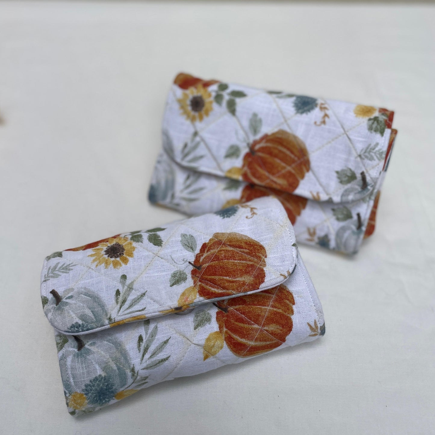 Two fabric pouches with pumpkin and sunflower pattern on a white surface