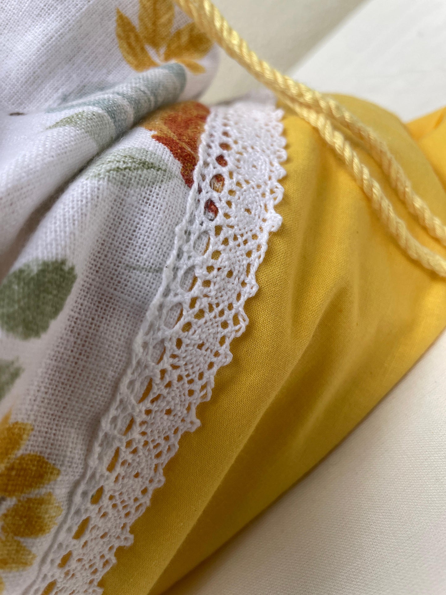 Close-up of a yellow drawstring bag with lace trim and a floral-patterned fabric inside.