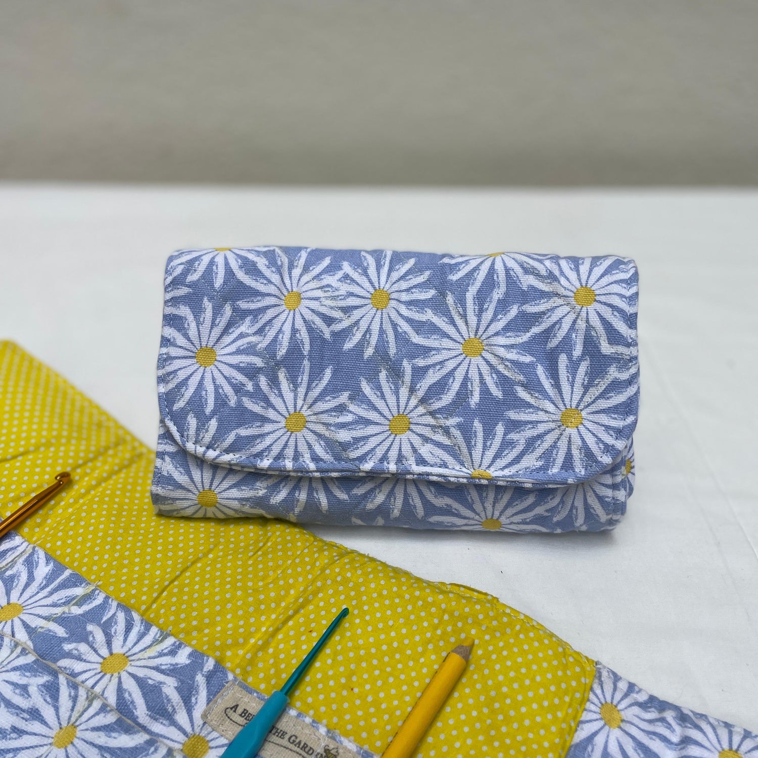 Fabric crochet hook roll with floral pattern and crochet tools on a white surface