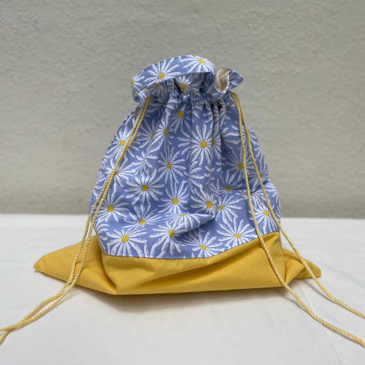 Drawstring bag with blue floral pattern and yellow drawstrings on a neutral background