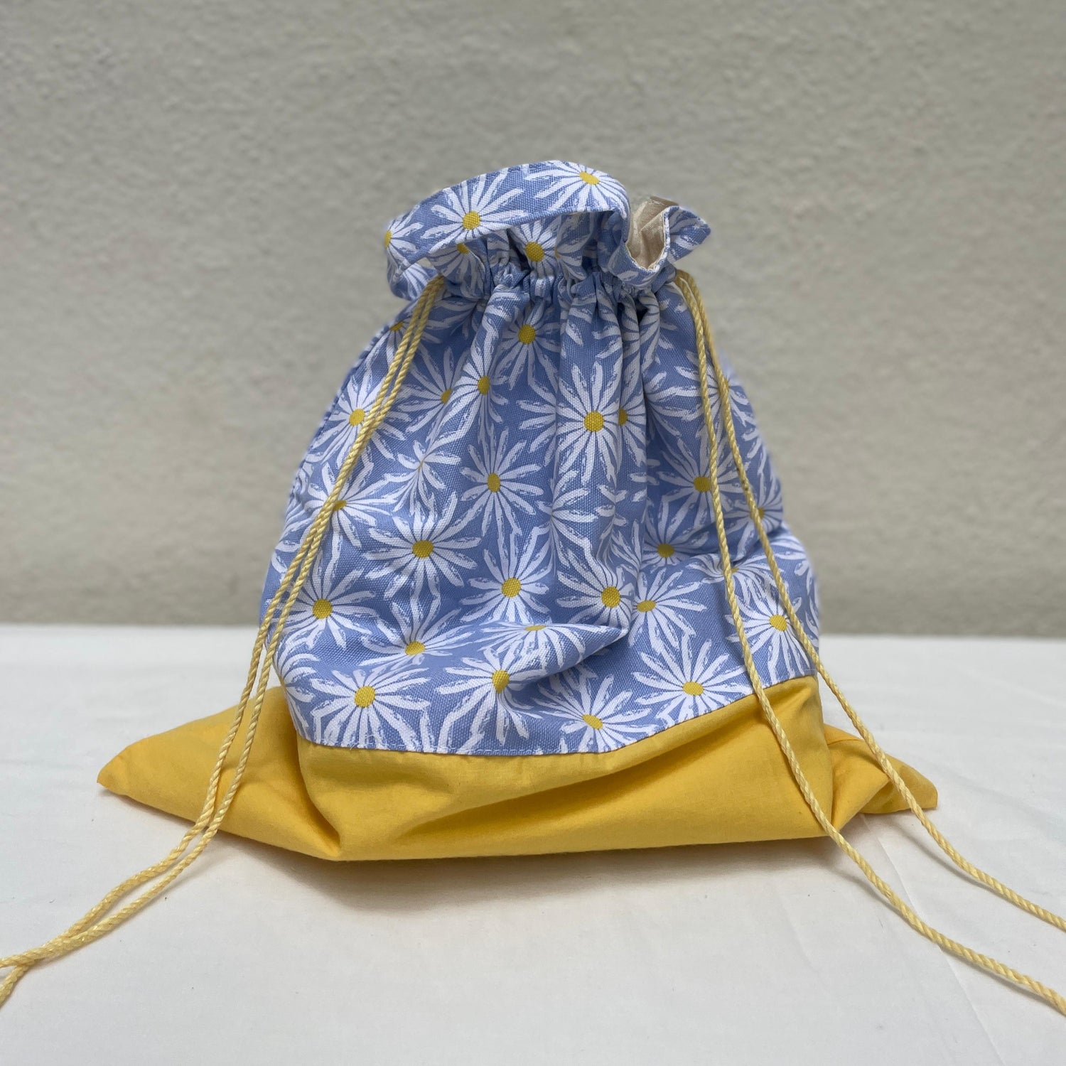 Drawstring bag with blue floral pattern and yellow drawstrings on a neutral background