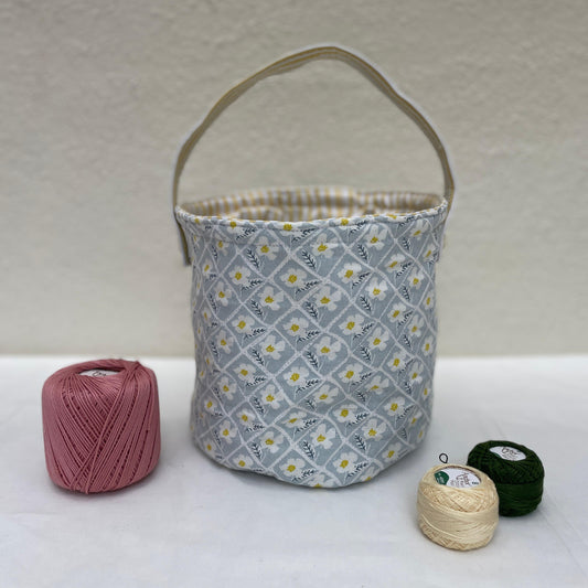 Fabric basket with floral pattern on a white surface with yarn balls.
