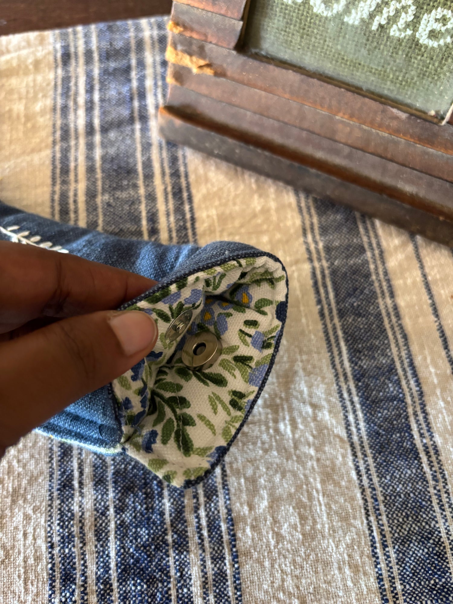 Heart-shaped fabric pouch with floral pattern held by a hand on a striped fabric background