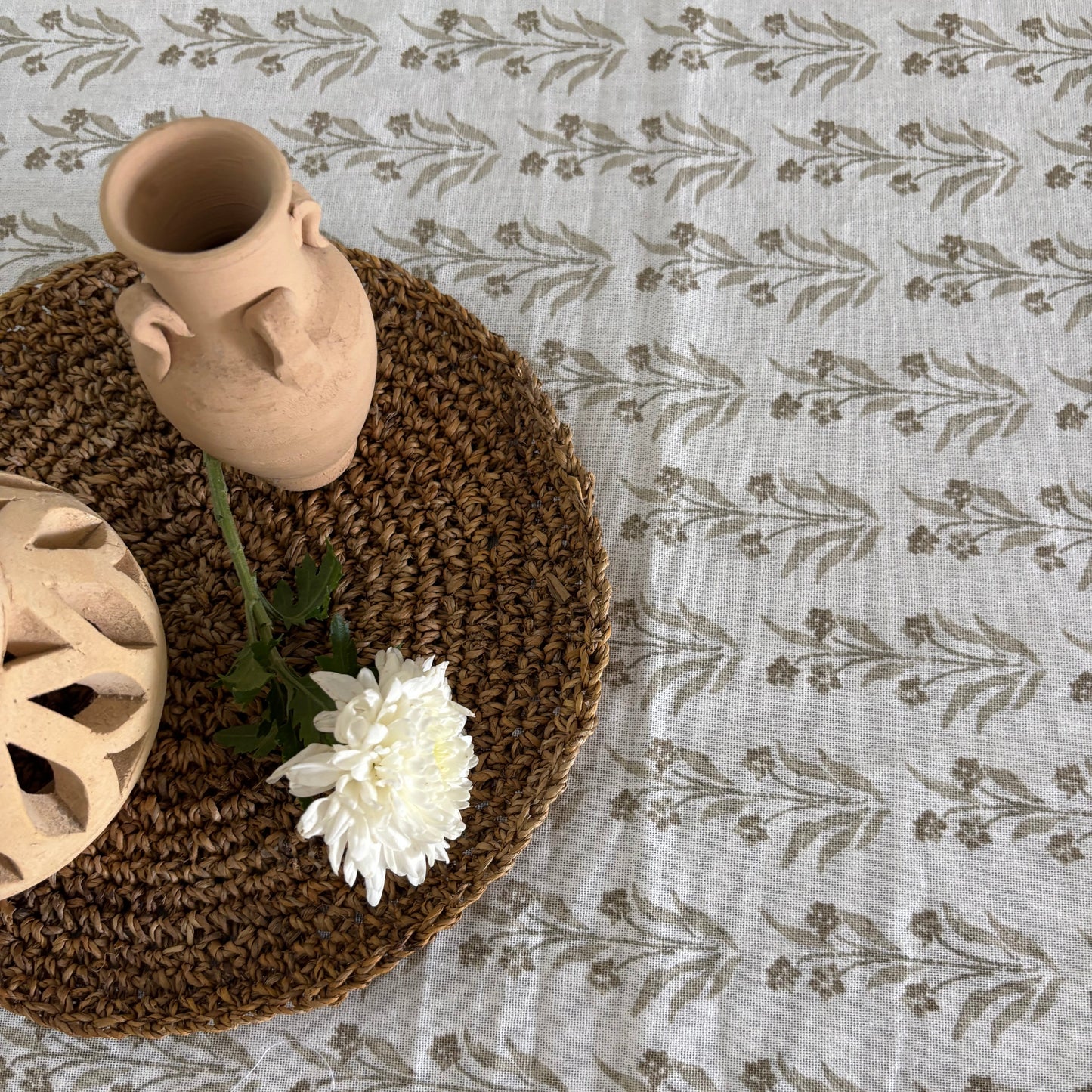 Decorative items on a dining table centre piece including a vase, a flower, and a textured mat on a patterned fabric table cover.