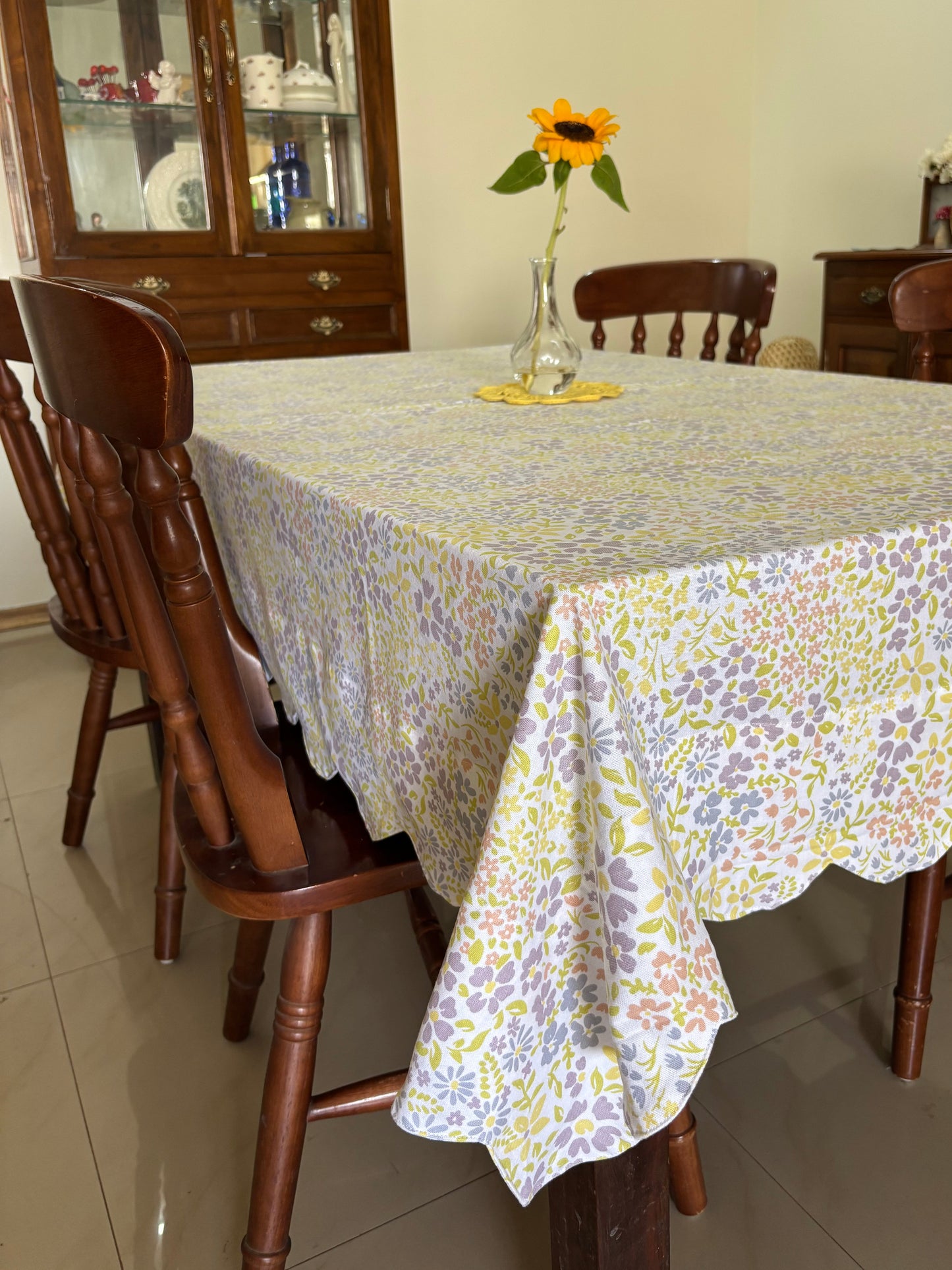 Dining table with a floral tablecloth and sunflower decoration, wooden chairs around it.