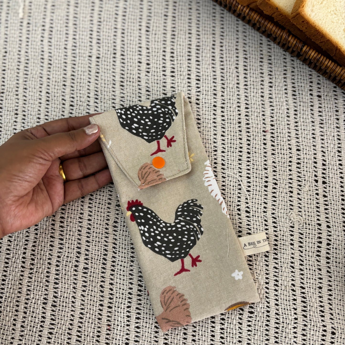 Hand holding a small fabric pouch with chicken design on a textured surface