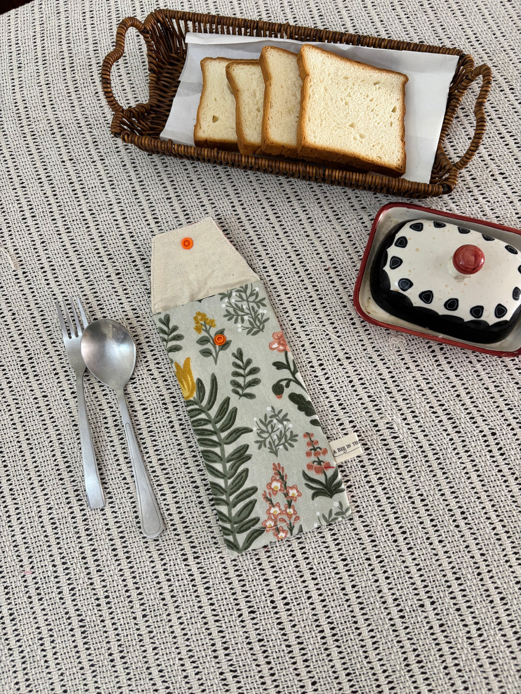 Bread slices in a basket, dessert in a bowl, and a floral-patterned knife on a textured surface.