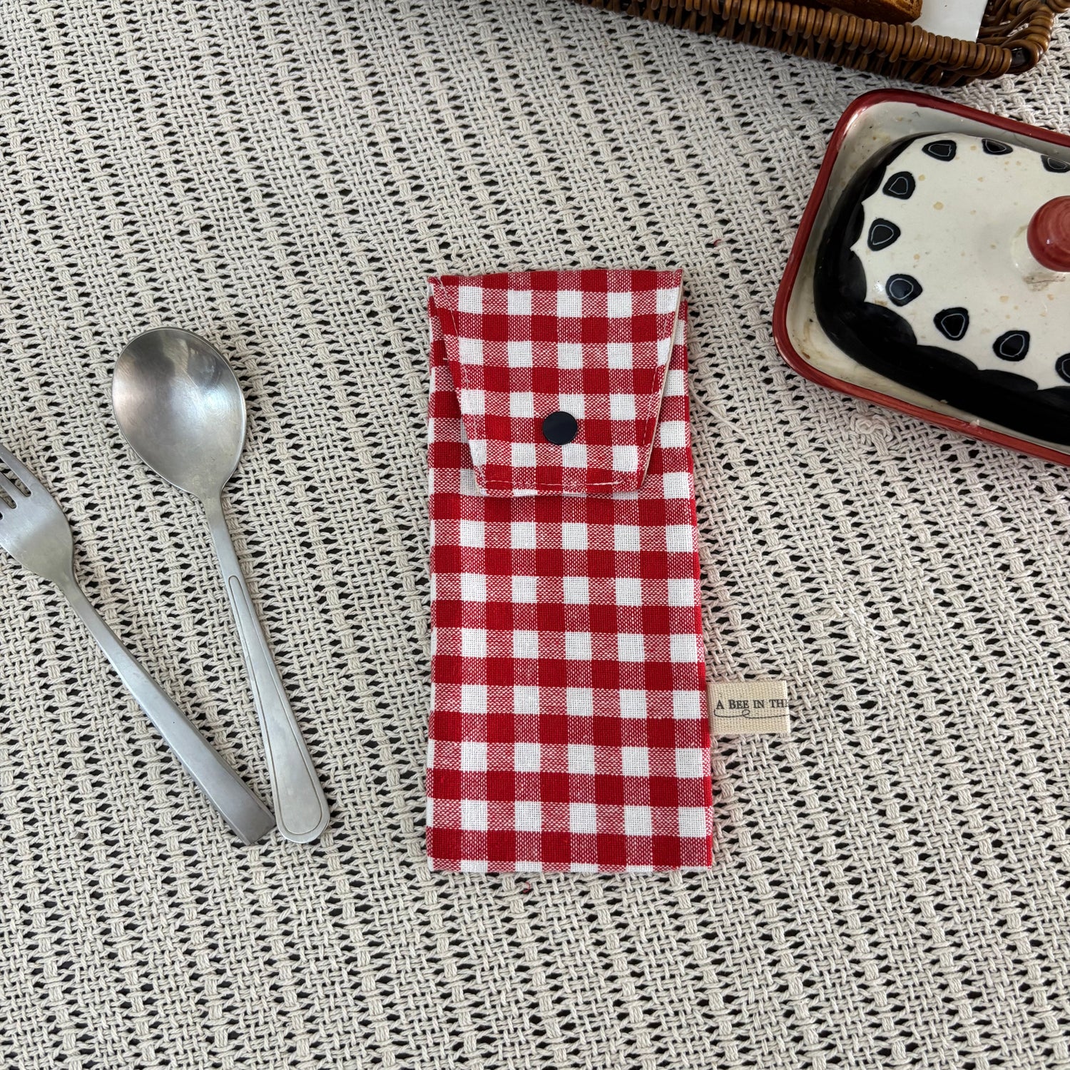 Red and white checkered napkin on a textured surface with bread and a jar in the background.