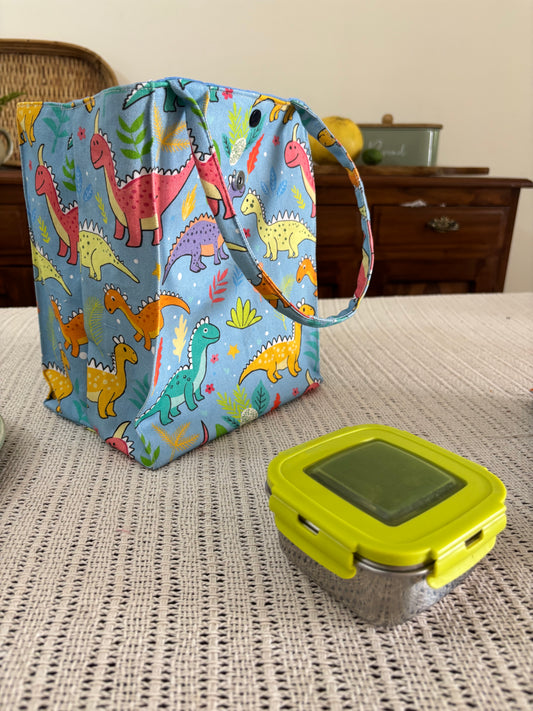 Colorful dinosaur-patterned bag and yellow digital device on a textured surface.