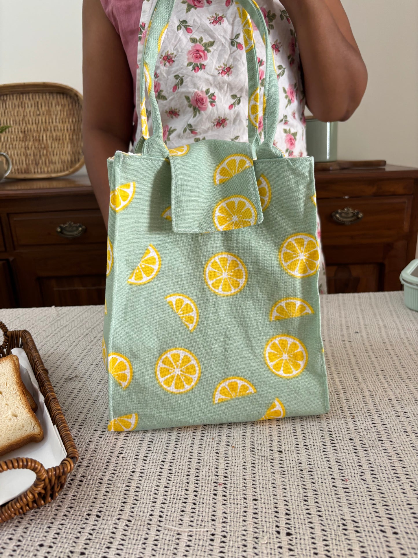 Person holding a green fabric with lemon pattern next to a textured wall.