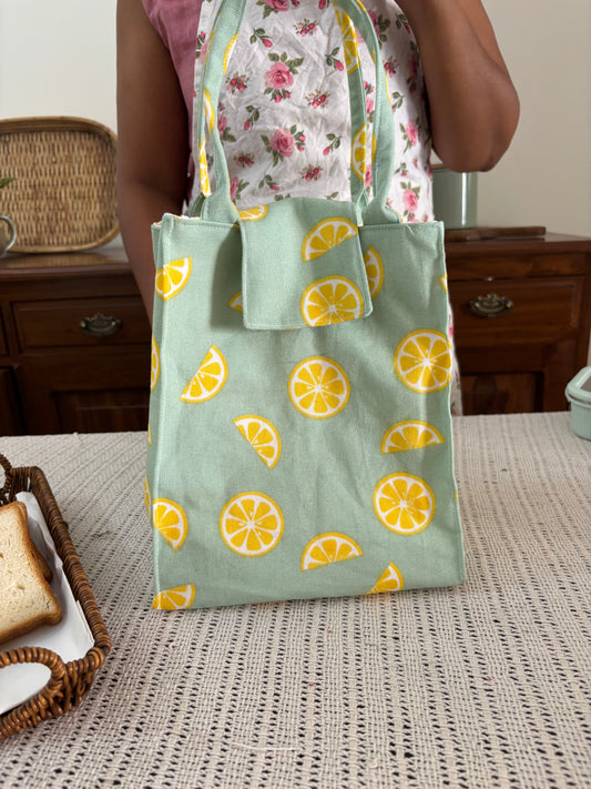 Person holding a green fabric with lemon pattern next to a textured wall.