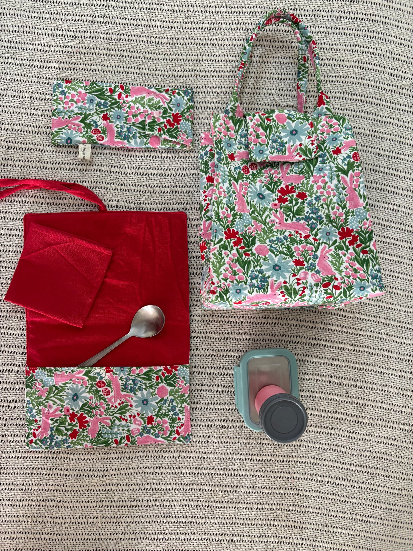 Floral-patterned bag and pouches with a red napkin and spoon on a textured surface