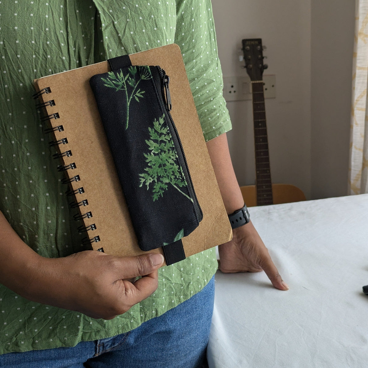 Black pouch with green leaf pattern and matching pen case on a notebook
