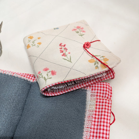 Folded fabric with floral pattern and red checkered border on a white background