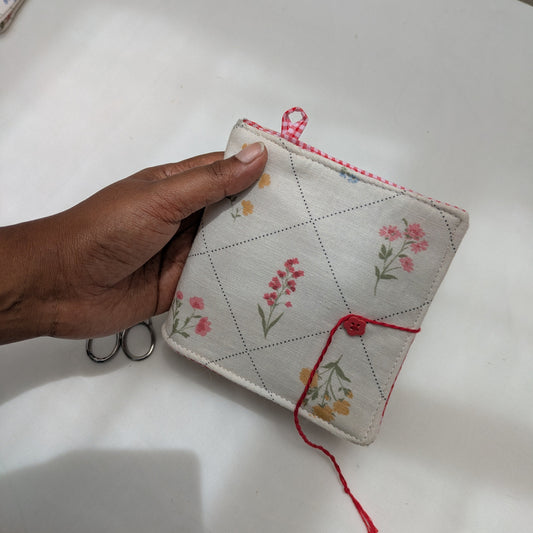 Hand holding a small needle book with floral patterns on a white surface.