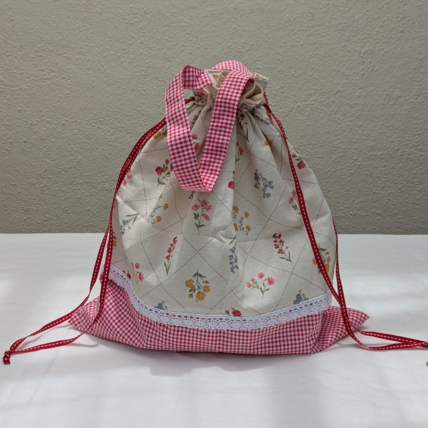 Person holding a floral-patterned bag with a pink drawstring on a street.