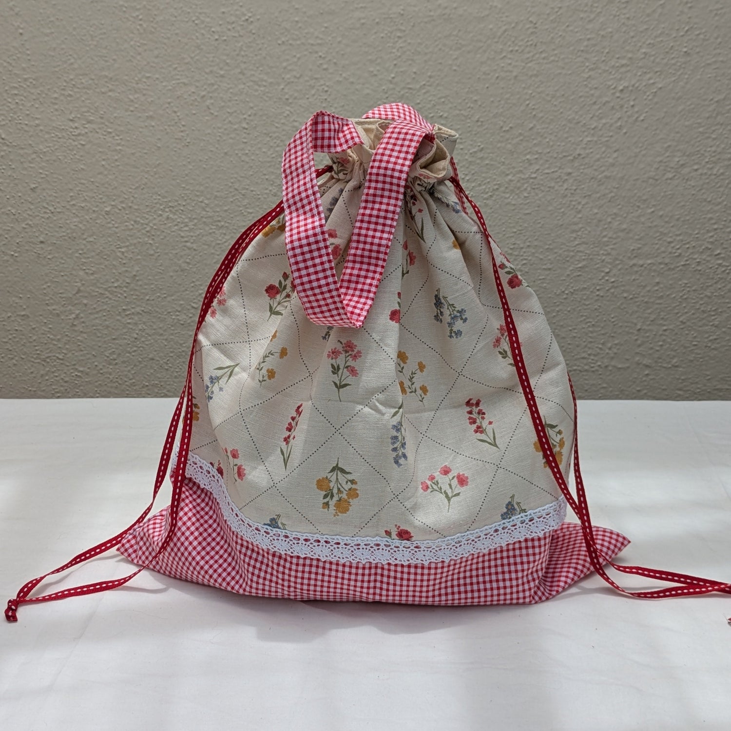 Person holding a floral-patterned bag with a pink drawstring on a street.