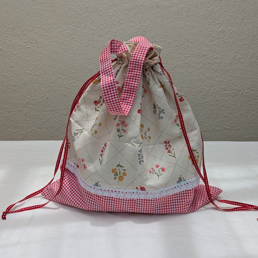 Person holding a floral-patterned bag with a pink drawstring on a street.