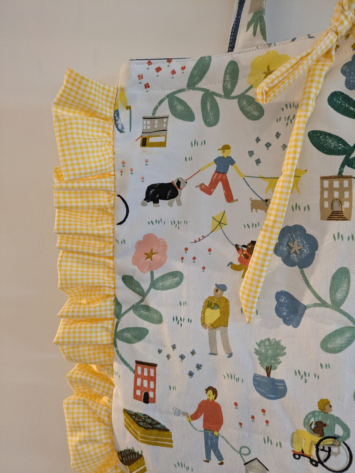Fabric with a colorful pattern of people and dogs on a yellow checkered border.