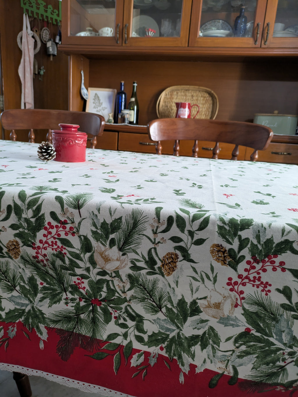 Dining room with a tablecloth featuring Christmas patterns and a wooden cabinet in the background.