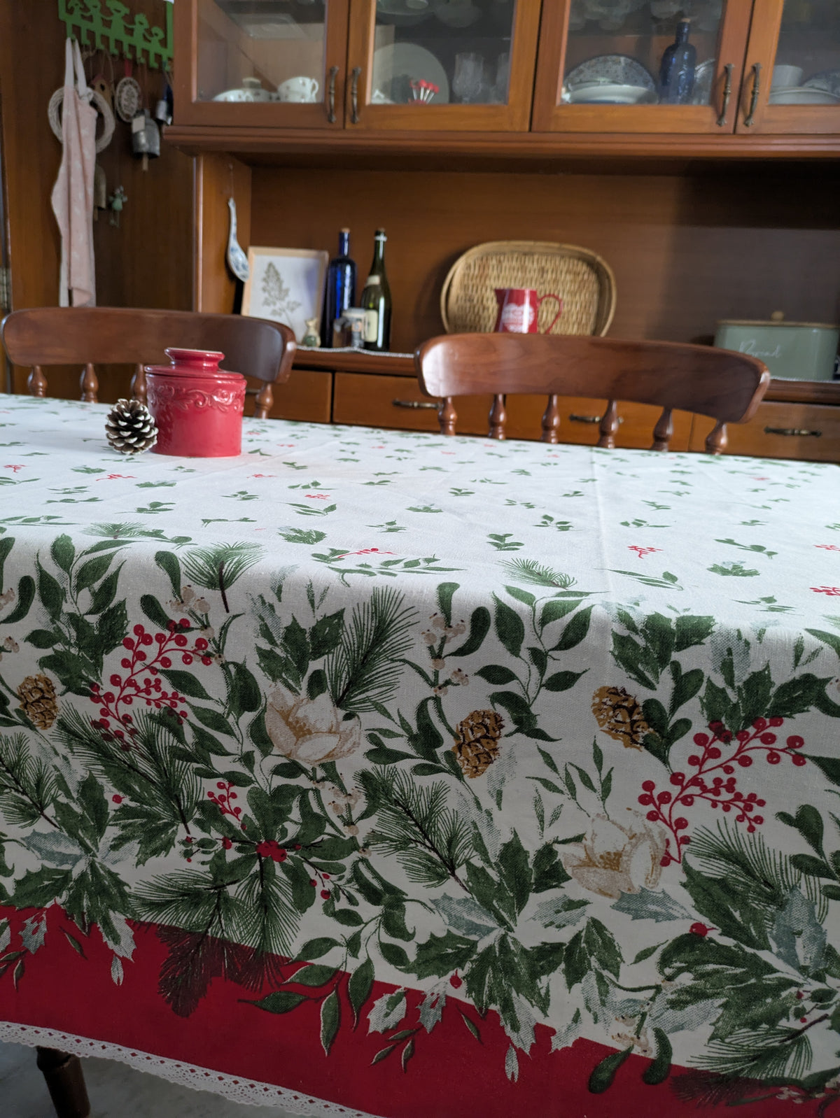 Dining room with a tablecloth featuring Christmas patterns and a wooden cabinet in the background.
