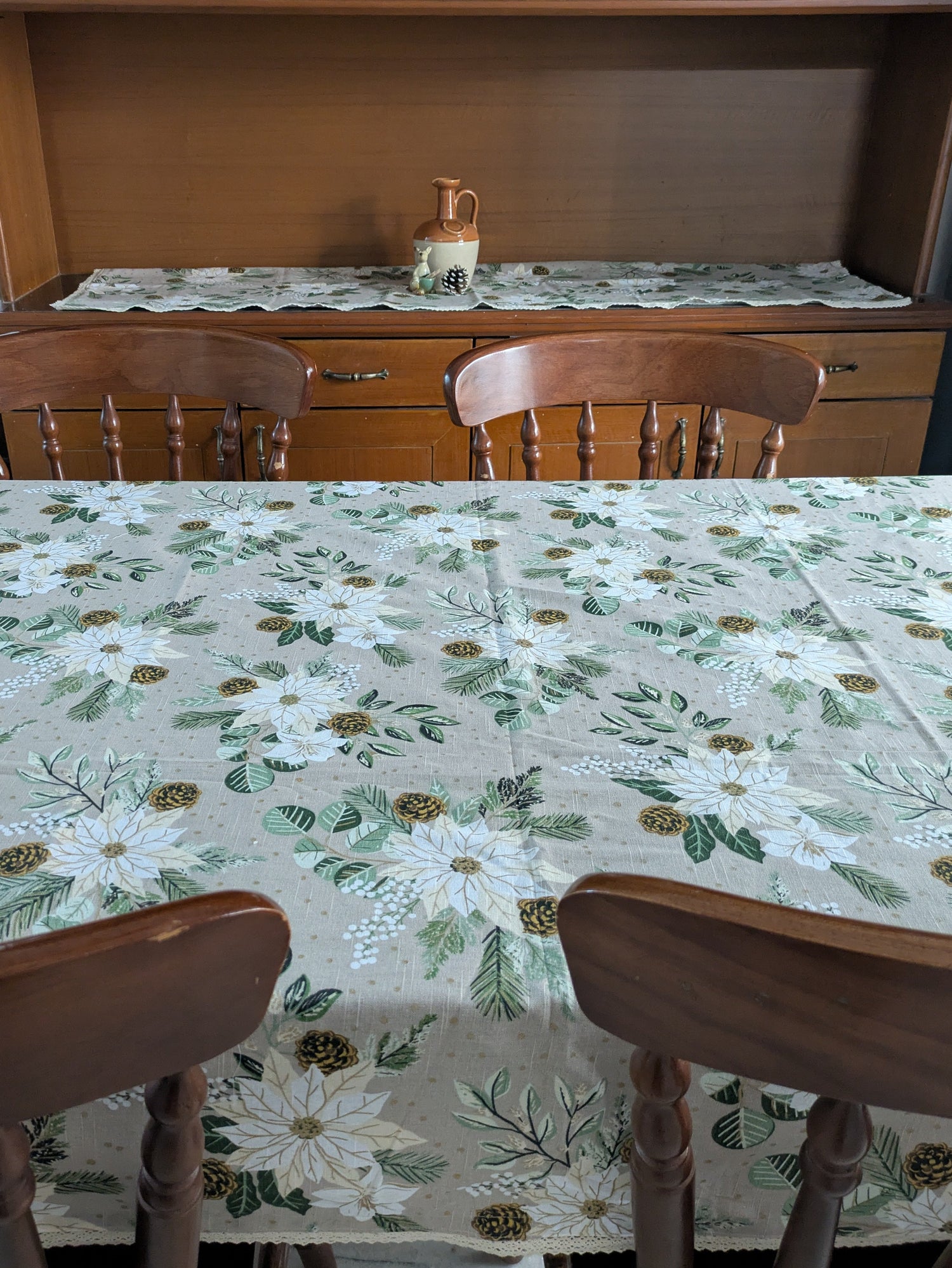 Dining room with floral tablecloth, wooden chairs, and a hutch.