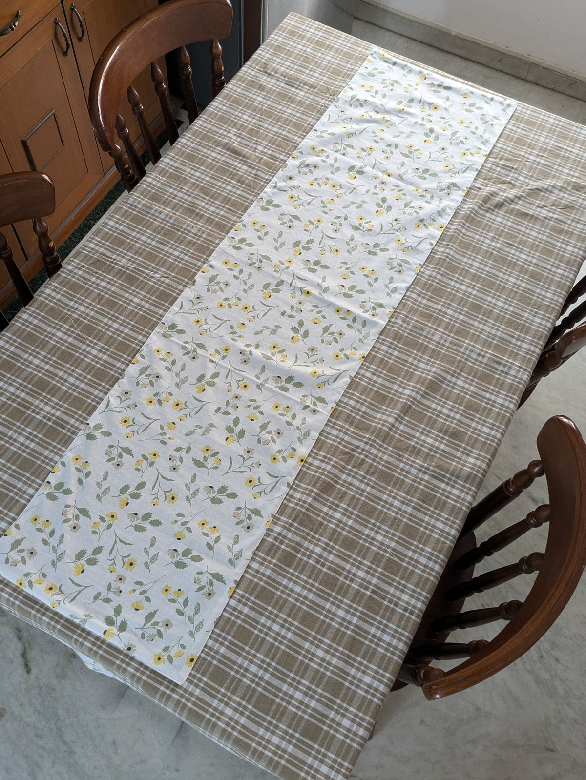 Table with a patchwork tablecloth featuring floral and plaid patterns, surrounded by wooden chairs.