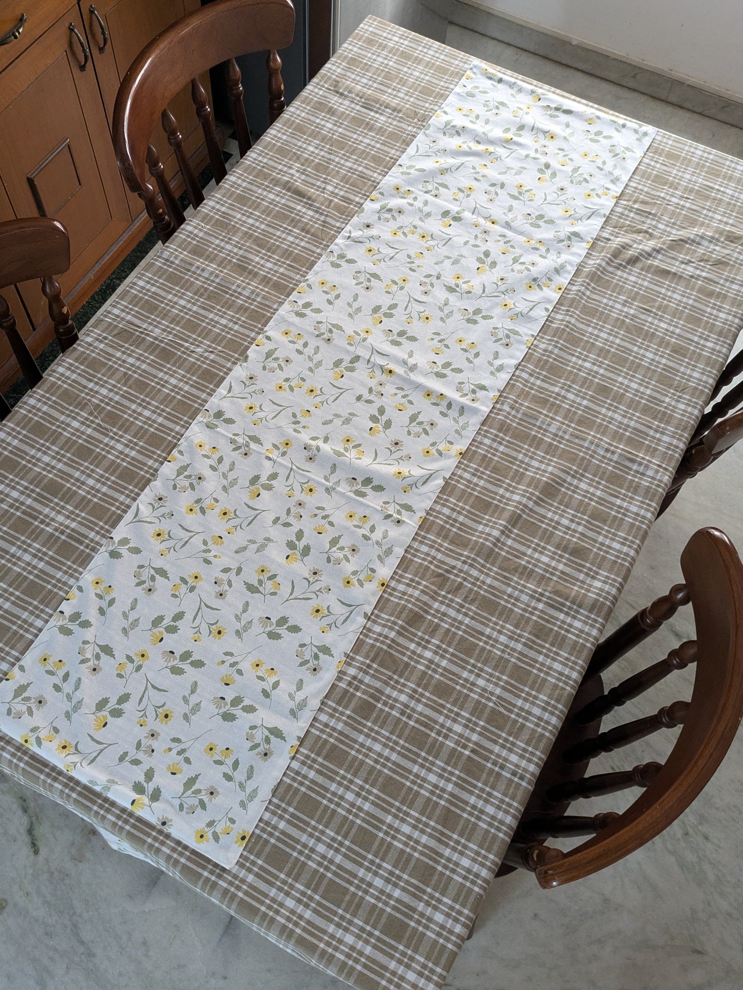 Table with a patchwork tablecloth featuring floral and plaid patterns, surrounded by wooden chairs.