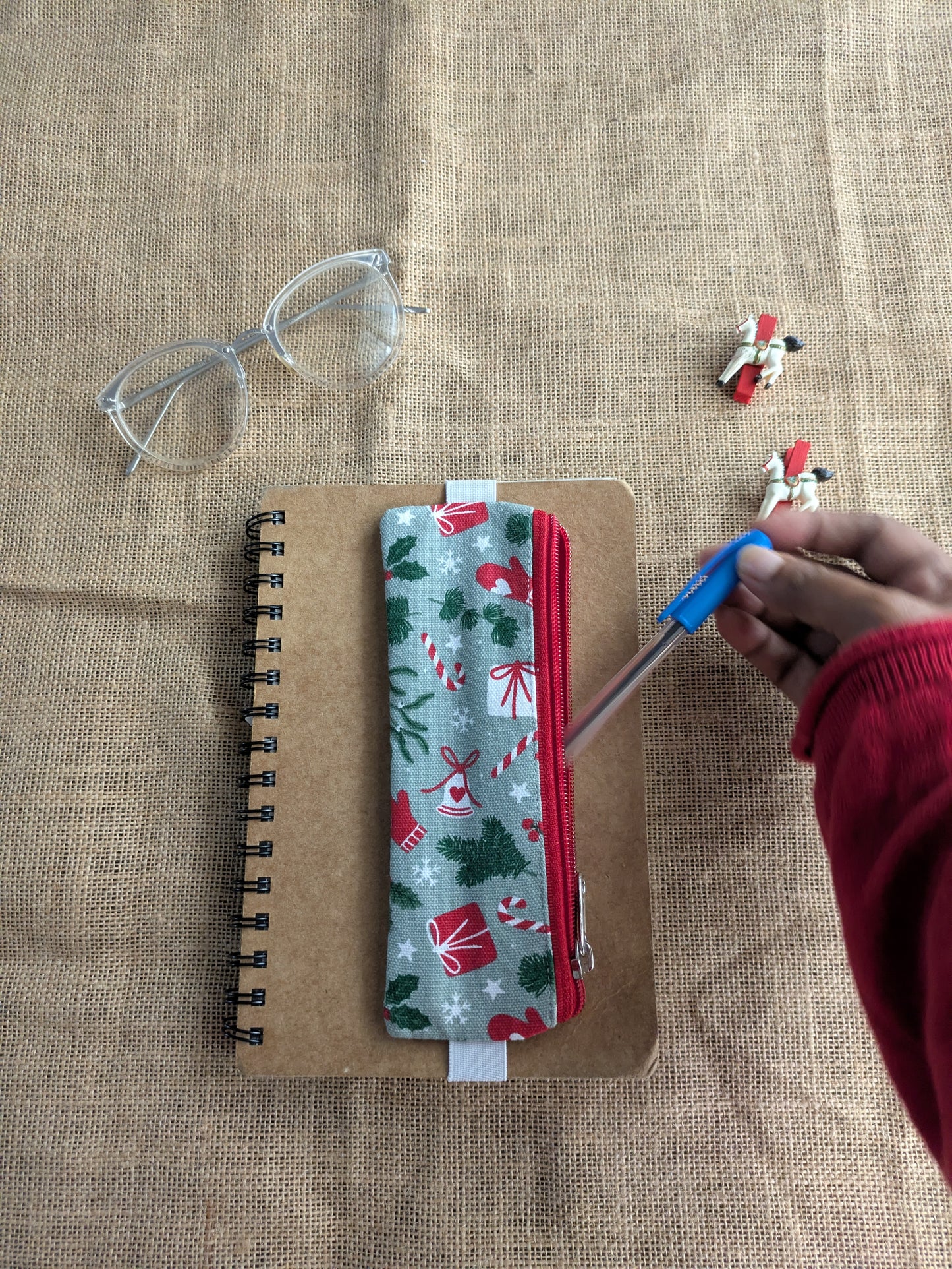 Notebook with a Christmas-themed pencil case and glasses on a textured surface.